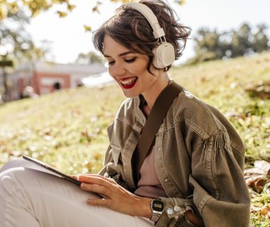 lovely-woman-jacket-headphones-sitting-grass-outdoors-happy-woman-with-curly-hairstyle-holding-smartphone-outside_197531-19354